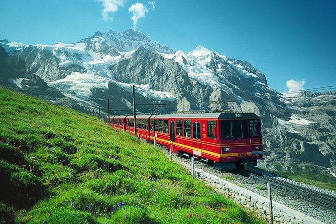 The red Jungfrau railway on a meadow below the Bernese Oberland peaks